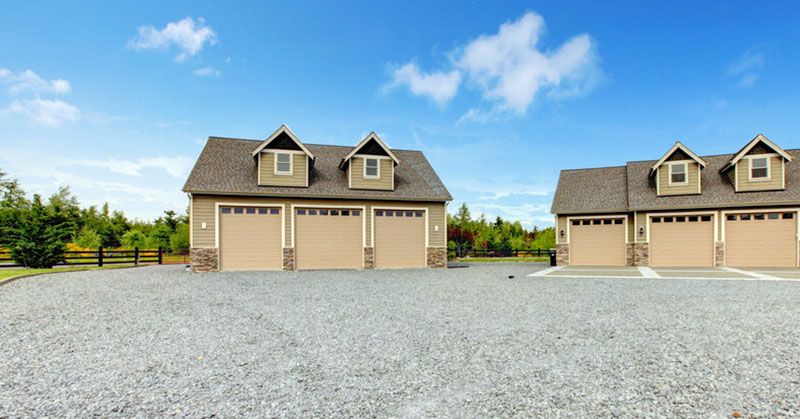 Two garages next to each other on a gravel driveway.