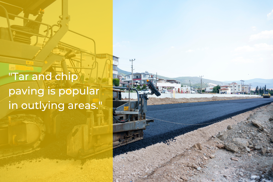 A tar and chip paving machine lays a new asphalt surface in a developing suburban area of Austin TX, with construction equipment and buildings visible in the background to help extend lifespan.